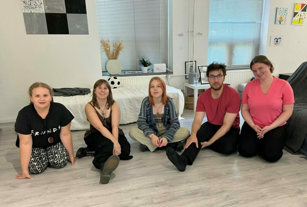 Kuvassa viisi PAUT Nuoret Aktivistit ryhmän jäsentä istuu lattialla kahden sohvan edessä.